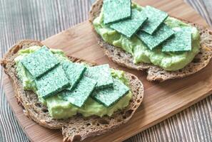 Slices of toasted bread with avocado paste and basil cheese photo