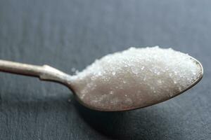 Spoon with white sugar on the dark background photo