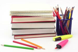 Crayon or colored pencils in box with side stack of books and school supplies on with background. Learning, study and office equipment concept. photo