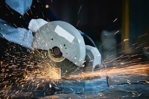 Heavy Industry Engineering Factory Interior with Industrial Worker Using Angle Grinder and Cutting a Metal Tube. Cutting metal and steel with a combination circular saw with a sharp round blade. photo