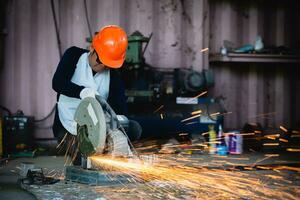 pesado industria Ingenieria fábrica interior con industrial trabajador utilizando ángulo amoladora y corte un metal tubo. corte metal y acero con un combinación circular Sierra con un agudo redondo cuchilla. foto