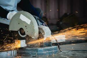 Heavy Industry Engineering Factory Interior with Industrial Worker Using Angle Grinder and Cutting a Metal Tube. Cutting metal and steel with a combination circular saw with a sharp round blade. photo