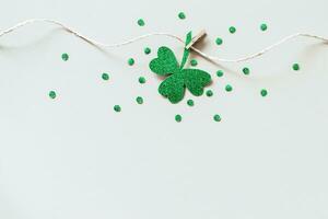 St. Patricks day background with Homemade glitter shamrocks garland. Shiny paper cut clover leaf on clothespin photo