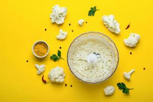 Blender bowl with freshly prepared cauliflower rice and spices on yellow background photo