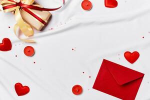 Romantic concept. Valentines day background. Red envelope, Gift box and hearts on white silk sheet photo