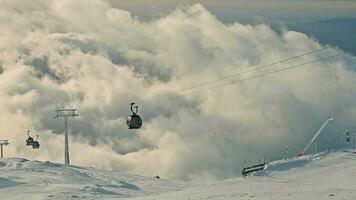 nublado céu sobre montanha gôndolas, gôndolas comovente através névoa sobre uma coberto de neve declive. video