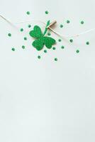 St. Patricks day concept. Glitter shamrocks garland. Shiny paper cut clover leaf on clothespin photo