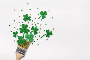 Creative St. Patricks Day concept made with paint brush and green glitter shamrocks and confetti. Minimal flat lay photo