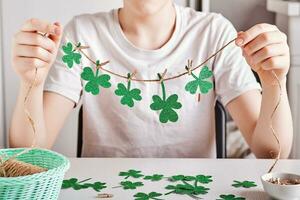 DIY St.Patricks Day decor. Happy boy make garland of shiny green paper. Selective focus photo