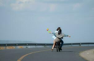 espalda ver de un joven mujer montando un bicicleta con su novio en el la carretera foto