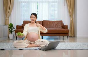 Pregnant woman eats salad as a snack while sitting on the floor of her home. photo