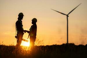 Silhouette of engineer and worker shaking hands on wind turbine background photo