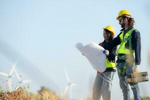 Engineer and worker discussing on a wind turbine farm with blueprints photo