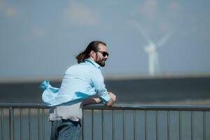 joven hombre relajante por el viento turbina en el lago foto