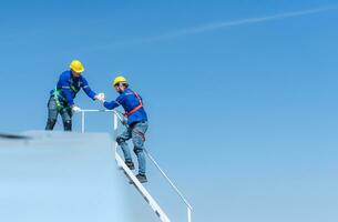 A young technician intern working on solar panels is fear of heights with senior engineers who are always helping out photo