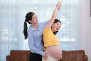 Happy Asian pregnant woman with yoga teacher teaching pregnancy yoga in her living room. photo