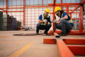 Portrait of two workers using digital tablet sit in front of the red steel structure photo