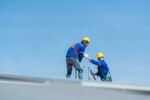 A young technician intern working on solar panels is fear of heights with senior engineers who are always helping out photo