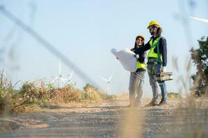 Engineer and worker discussing on a wind turbine farm with blueprints photo