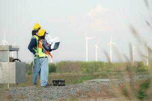 Engineer and worker discussing on a wind turbine farm with laptop photo