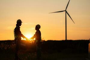 Silhouette of engineer and worker shaking hands on wind turbine background photo