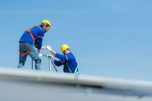 A young technician intern working on solar panels is fear of heights with senior engineers who are always helping out photo