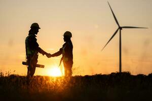 Silhouette of engineer and worker shaking hands on wind turbine background photo