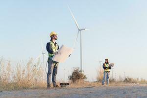 joven hombre ingeniero vistiendo la seguridad casco y participación Plano en viento turbina granja. foto