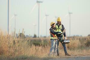 Engineer and worker discussing on a wind turbine farm with laptop photo