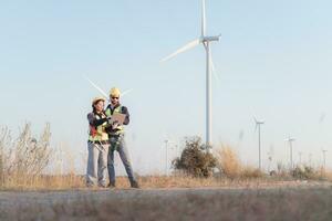 Engineer and worker discussing on a wind turbine farm with laptop photo