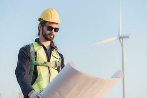 joven hombre ingeniero vistiendo la seguridad casco y participación Plano en viento turbina granja. foto