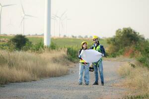 Engineer and worker discussing on a wind turbine farm with blueprints photo