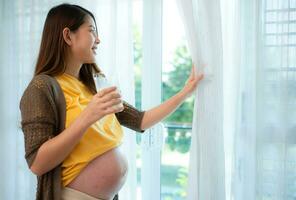 Pregnant asian woman holding glass of milk and smiles happily talking to her unborn child. photo
