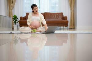 Pregnant woman eats salad as a snack while sitting on the floor of her home. photo