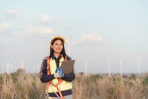 hembra ingeniero vistiendo la seguridad casco y participación ordenador portátil en viento turbina granja. foto