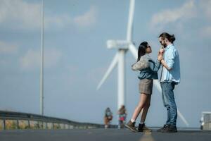 On the road, a young couple proposes to each other, with wind turbines in the background. photo