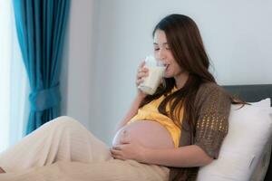 Portrait of beautiful asian pregnant woman drinking milk in bedroom at home photo