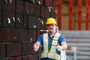 Portrait of a construction worker standing with thumbs up in front of steels material wall photo