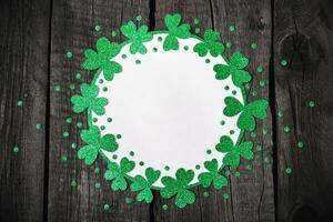 St. Patricks Day background. Round frame of shiny shamrocks and confetti on rough wooden background photo