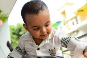 bebé chico a hogar balcón. brillante retrato de contento niño sentado en el mesa. pequeño 1 año antiguo chico durante el día ligero a casa balcón. foto