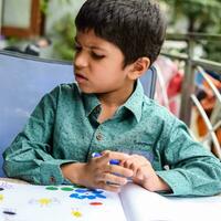 Smart Indian little boy perform thumb painting with different colourful water colour kit during the summer vacations, Cute Indian Kid doing colourful thumb painting drawing on wooden table photo