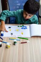 Smart Indian little boy perform thumb painting with different colourful water colour kit during the summer vacations, Cute Indian Kid doing colourful thumb painting drawing on wooden table photo