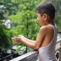 Little kid playing in summer rain in house balcony, Indian smart boy playing with rain drops during monsoon rainy season, kid playing in rain photo