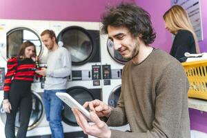 group of addicted friends are playing with tablets and smartphones in a public laundry photo