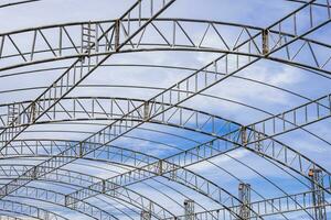 Curve lines pattern of metal roof beam structure of large dome event tent against clouds on blue sky background photo