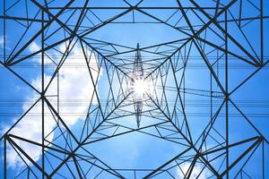 Silhouette bottom view of high voltage tower with power lines against cloud on blue clear sky background in sunny day photo