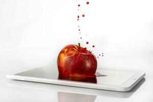 red apple is sinking into the viewer of a tablet on white background photo