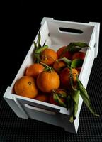 wooden box full of tangerines with green leaves photo