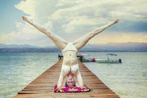 young woman does handstands on a wooden dock photo