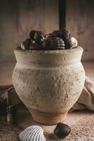 shell shaped chocolates with cream in a clay jar photo